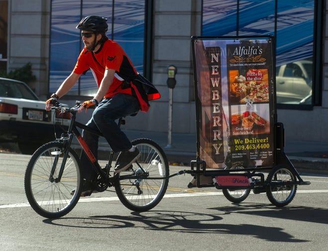 Nick Smith with the new Stockton ad startup Road Finch, rides a bike pulling an advertising sign on Main Street near San Joaquin Street. CLIFFORD OTO/THE RECORD