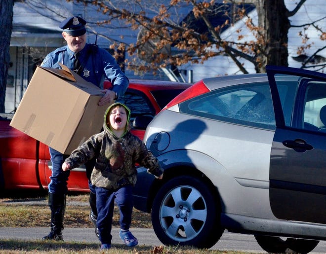 State Trooper Michael Lokaitis follows Aidyn Wirf to the car so he can put a box filled with a Christmas meal inside. The state police union and troopers from the Brookfield barracks delivered the meals to the St. Mary's Church food pantry Saturday. T&G Staff/Kim Ring