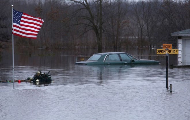 A submerged automobile can be seen in front of a residence at the intersection of Division and Springfield streets along with submerged Christmas decorations snagged on the base of the American flag seen in Kincaid on Wednesday, Dec. 30, 2015. In Kincaid, which sits near the South Fork of the Sangamon River, floodwaters closed a section of Illinois 104, with a section of homes in South Kincaid along Springfield St. surrounded by water cut off. Volunteers using atv's ferried supplies into the area for homes that still had power not affected by the flooding. David Spencer/The State Journal-Register