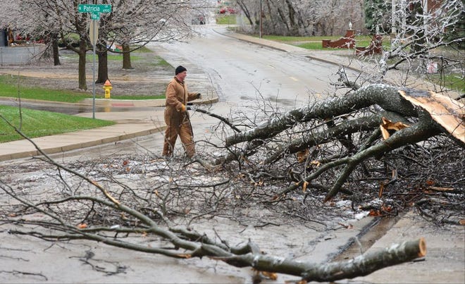 Anthony Jones jumps in to help out neighbors clear a tree out of the street on Teton Drive after freezing rain and powerful wind gusts hammered the Peoria area on Monday.