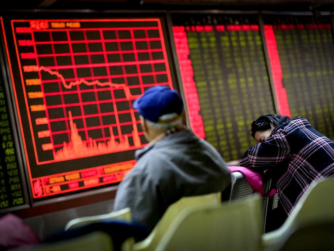 A woman takes a nap as a man looks at an electronic board displaying stock prices at a brokerage house in Beijing on Monday.