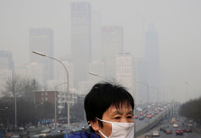 In this Dec. 20, 2015, file photo, a woman wearing a mask for protection against pollution walks on a pedestrian overhead bridge as office buildings in Central Business District of Beijing are shrouded with smog. Environmental authorities in Beijing said the Chinese capital's air quality in 2015 was better than the year before despite the city's first two red alerts for pollution late in the year. China has been setting national and local targets to reduce its notorious air pollution as citizens have become increasingly aware of the health dangers. (AP Photo/Andy Wong, File)