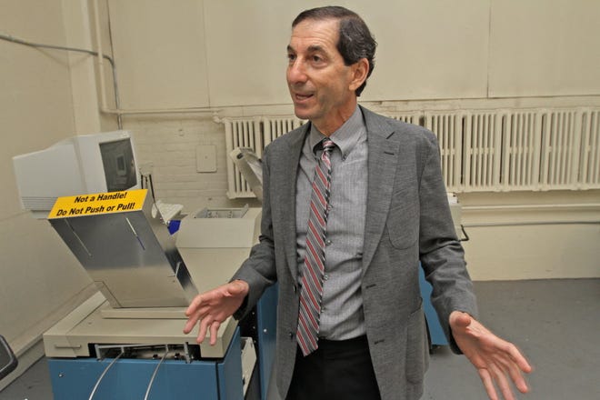 Robert Kando, executive director of the Board of Elections, stands beside a high- speed reader the state uses for counting mail-in ballots in October 2014.