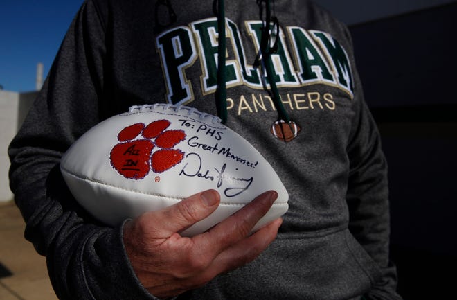In this Tuesday, Jan. 5, 2016, photo, Pelham High School head coach Tom Causey stands outside of his office holding a football that was given to him and signed by Clemson football head coach Dabo Swinney, who attended Pelham High School, in Pelham, Ala. Swinney has a reputation as a faithful, determined guy who married his high school sweetheart and hasnít forgotten the folks back home. When Tom Causey was hired as Pelhamís football coach a year ago, Swinney got in touch.ìHe called and wished me well,î said Causey, whose brother played at Alabama with Swinney. ìHe absolutely loves Pelham.î Clemson will now play Alabama in the NCAA college football championship game on Monday. (AP Photo/Brynn Anderson)