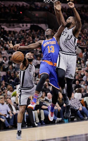New York Knicks guard Jerian Grant (13) drives between San Antonio Spurs defenders Patty Mills (8) and Jonathon Simmons (17) during the first half of an NBA basketball game Friday, Jan. 8, 2016, in San Antonio. Grant was fouled on the play. (AP Photo/Eric Gay)