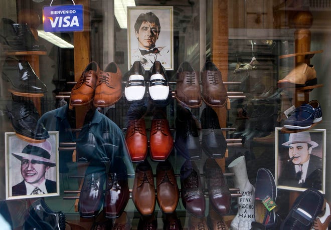 FILE - This Thursday, Jan. 22, 2015 file photo shows portraits of actor Al Pacino as character Tony Montana, center, gangster Al Capone, right, and Latin American tango icon Carlos Gardel, left, in a display in a men's shoe store in downtown Lima, Peru. The store owner said he sells shoe styles that these famous men and character used. (AP Photo/Esteban Felix)