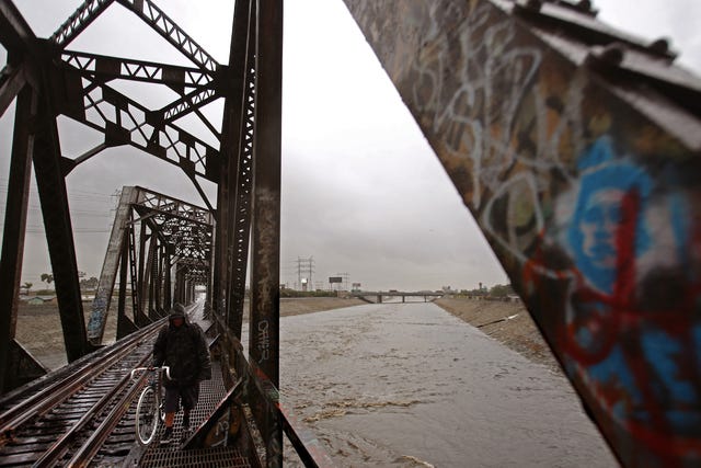 A man walks along an old Union Pacific Bridge as the Los Angeles River flows Wednesday, Jan. 6, 2016, in South Gate, Calif. (Los Angeles Times) 
 Trash piles up on the banks of the Los Angeles River after a heavy rainstorm passed through the area, raising the water levels in the river Tuesday, Jan. 5, 2016, in Vernon, Calif. (Los Angeles Times)