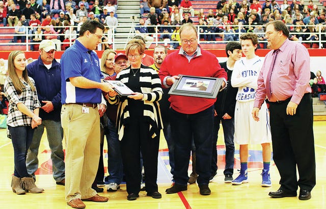 The widow of the late Jim Spears accepts a plaque from Mt. Pleasant assistant principal Eric Hughes (left), while Jim's son Tim admires a framed picture presented by Mt. Pleasant athletic director Webb Williams (right) during a presentation at halftime of last Friday's Columbia Academy at Mt. Pleasant boys basketball game. Family members are pictured in the background. (Photo by correspondent Rob Fleming)