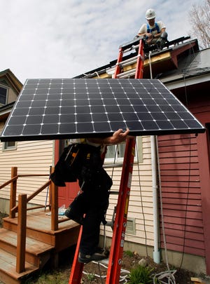 In this April 29, 2013, file photo, Jon Kirkpatrick carries a solar panel up to Bevan Walker for an installation for SunCommon in Montpelier, Vt. The Vermont attorney general's office issued a warning letter to solar industry players in December 2015 saying some could face penalties for deceptive advertising if they are not clear when consumers are buying electrons but not environmental benefits. SunCommon, Vermont's largest seller of community solar, is taking renewable energy credits tied to community solar projects and selling those credits to utilities in Massachusetts and Connecticut so they can meet state renewable energy quotas. It's commonplace and legal for companies and governments to swap energy credits. (AP Photo/Toby Talbot, File)