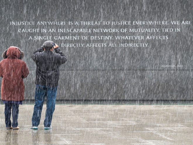 Visitors at the Martin Luther King, Jr. Memorial in Washington stop to photograph the quotes etched into the memorial's back wall while it snows in the nation's capital on Sunday.