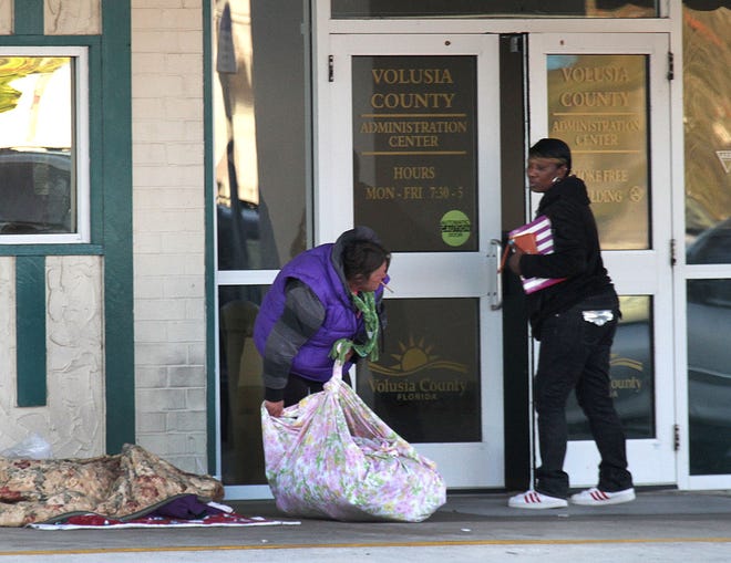 A person entering the Volusia County Administration Center looks at a homeless woman picking up her belongings from in front of the door where she camped the previous night. News-Journal/David Tucker