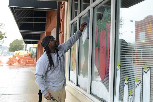 Vachon Harrison removes the Christmas scenes painted on the windows at the Kinston Enterprise Center on Friday. Harrison, originally from Connecticut, says the people in Kinston are friendlier than the other places he works.