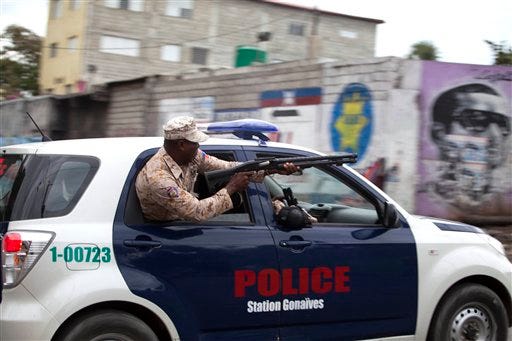 A national police officer fires birdshot at demonstrators during a street protest after it was announced that the runoff Jan. 24, presidential election had been postponed, in Port-au-Prince, Haiti, Friday, Jan. 22, 2016. The Provisional Electoral Council in Haiti has postponed the election amid escalating protests by the opposition, which claims the first round was marred by fraud in favor of a government-backed candidate. (AP Photo/Dieu Nalio Chery)