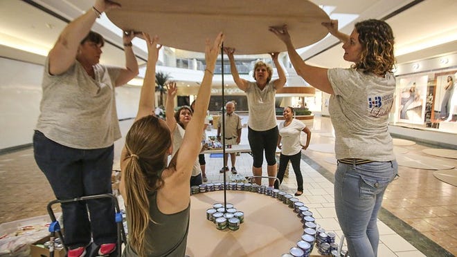 (l-r) Hedrick Brothers Construction team members (l-r) Tanya Stiles, Alex Roeder, Yolanda Donado, Wanda Stan, and Daniela Wogh work to position a piece of plywood that will be used to help stabilize the globe they are constructing out of cans June 7, 2015 during Canstruction 2015 at The Gardens Mall. The Hedrick team was one six teams participating in the event which was held to benefit The Palm Beach County Food Bank. “We believe that helping to relieve hunger begins right here in Palm Beach County,” said Christine Corrigan of the Hedrick team. (Damon Higgins / The Palm Beach Post)