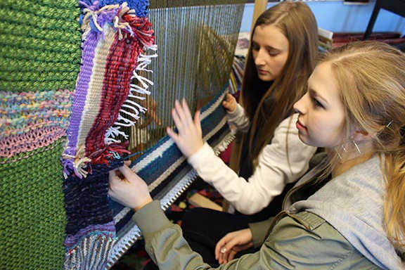 Ally Muzyka, left, and Lily McKay, sophomores, weave knitted squares into a shawl.