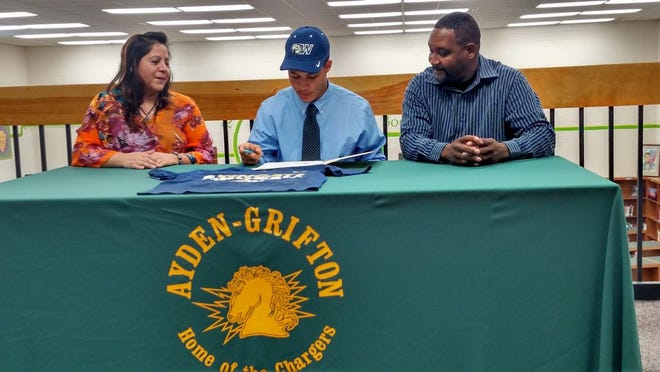 Ayden-Grifton's Michael Baker Jr., center, wears a Wingate University hat while signing a document, accompanied by his mother, Gabriella Baker, and father, Michael Baker Sr., Wednesday in the Ayden-Grifton Media Center. Baker Jr. committed to Wingate University as a running back and defensive back.