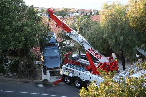 A crane removes a car that crashed off Palos Verdes Drive west and ended up on the roof of a home in Palos Verdes Estates, Calif. Wednesday, Feb. 3, 2016. Firefighters pulled the man from the damaged car and took him to a hospital, but he wasn’t seriously hurt, and no one else was injured. (Chuck Bennett/Daily Breeze via AP)
