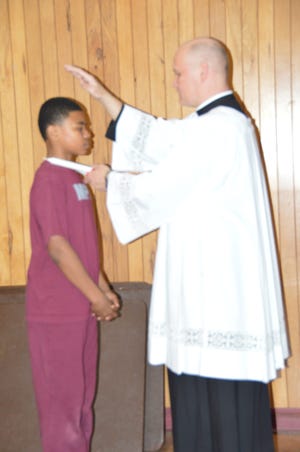 The Rev. Tom Roslak of Most Precious Blood Parish uses a consecrated candle as he blesses the throat of a student during Most Precious Blood School’s recent celebration of St. Blaise. Photo provided