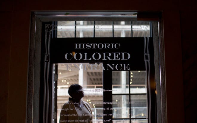 In this Thursday, Jan. 7, 2016 photo, a woman stands in the doorway of then new Historic Colored Entrance at the Lyric Theatre, in Birmingham, Ala. Preservationists had to decide whether to keep reminders of The Lyric’s discarded color line before they unveiled an $11 million restoration of the 102-year-old theater, which had been closed for decades. In this case, they chose to highlight the history, installing a glass door with the etched words “Historic Colored Entrance” in the lobby wall so patrons can peer into the past. (AP Photo/Brynn Anderson)