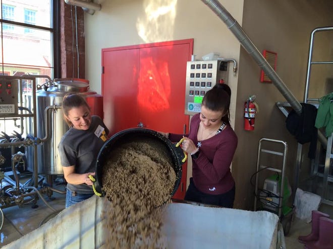 Two members of the Greenville chapter of Girls Pint Out empty a bucket of spent grain while brewing their Free Hugs Pale Ale at Mother Earth Brewing in January.