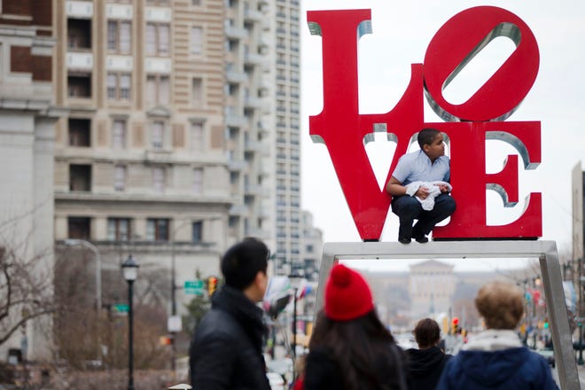 In this March 27, 2015, file photo, a young man climbs on a sculpture by Robert Indiana, at JFK Plaza, commonly known as Love Park, in Philadelphia. On Wednesday, Feb. 10, 2016, city officials broke ground on a $16.5 million, yearlong renovation of the park, requiring a temporary relocation of the park's Robert Indiana sculpture, expected to receive about four months of restoration work. (AP Photo/Matt Rourke)