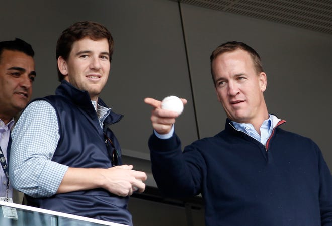 FILE - In this May 4, 2014, file photo, Denver Broncos quarterback Peyton Manning, right, points out something in the stadium to his brother, New York Giants quarterback Eli Manning, from New York Yankees' Derek Jeter's suite during a baseball game between the Yankees and the Tampa Bay Rays at Yankee Stadium in New York. Peyton Manning had a little fun with little brother Eli's sad face at the Super Bowl during an appearance on NBC's "Tonight Show." (AP Photo/Kathy Willens, File)