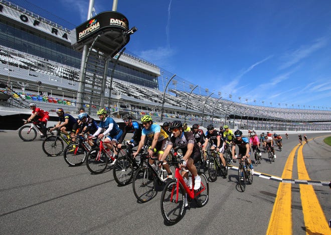Jimmie Johnson, Trevor Bayne and other drivers cross the start finish line after a 60-mile ride from St. Augustine to Daytona International Speedway to promote biking safety Wednesday. News-Journal/JIM TILLER