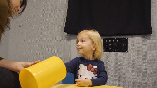 In this images from video provided by University of North Carolina at Chapel Hill, a toddler participates in a speech perception experiment in a laboratory at the University of North Carolina in Chapel Hill, N.C.. The toddler was conditioned to put a block in the bucket whenever she heard the "target" word. From the cacophony of day care to the buzz of TV and electronic toys, noise is more distracting to a child's brain than an adult's, and new research shows it can hinder how youngsters learn. In fact, one of the worst offenders when a tot's trying to listen is other voices babbling in the background, researchers said Saturday at a meeting of the American Association for the Advancement of Science. (Emily Buss/University of North Carolina at Chapel Hill via AP)