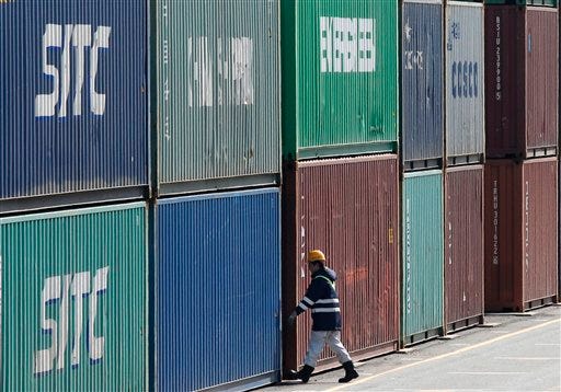 A port worker walks through the piled containers in Tokyo, Thursday, Feb. 18, 2016. Japan's trade balance returned to deficit in January, with a shortfall of 646 billion yen ($5.65 billion) as exports fell 13 percent from the year before, led by an 18 percent plunge in the value of shipments to China.