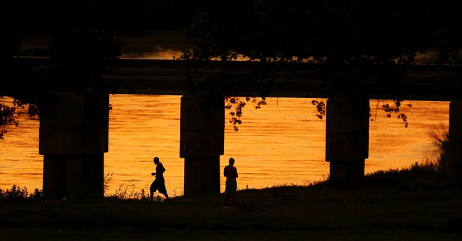 People are silhoutted against the setting sun’s colors reflected in the Arkansas River as they walk along the riverbank June 2, 2015, in Hutchinson’s Carey Park.