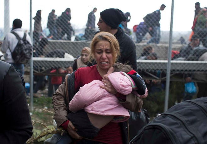 A woman carries a child on the Greek side of the border as they run away after Macedonian police fired tear gas at a group of the refugees and migrants who tried to push their way into Macedonia, breaking down a border gate near the northern Greek village of Idomeni on Monday, Feb. 29, 2016. No arrests or injuries were reported. About 6,500 migrants are stuck on the Greek-Macedonian border at Idomeni, waiting to travel north, but Macedonia is only admitting a trickle.(AP Photo/Petros Giannakouris)