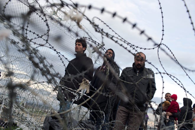 Refugees look at the the border crossing in front to a wire fence that separates the Greek side from the Macedonian one at the northern Greek border station of Idomeni, Thursday, March 3, 2016. More than 10,000 mostly Syrian and Iraqi refugees were stuck at the country's Idomeni border crossing in deteriorating conditions. (AP Photo/Petros Giannakouris)