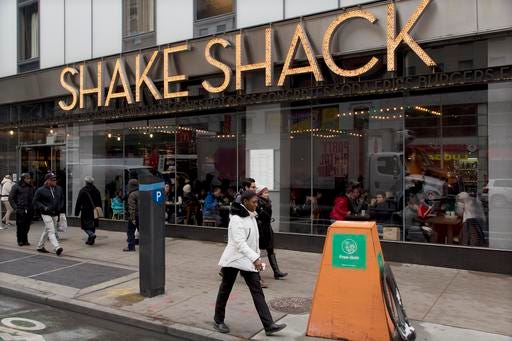 In this Friday, March 4, 2016, photo, people walk past a Shake Shack in New York. The New York-based restaurant chain has more than 60 locations worldwide. The company reports earnings, Monday, March 7. (AP Photo/Mark Lennihan)
