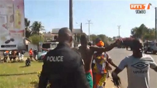 In this image made available by RTI via Associated Press television people is being searched by a police officer after an attack in Grand-Bassam, Ivory Coast, Sunday March 13, 2016. At least six armed men attacked beachgoers outside three hotels Sunday in Grand-Bassam, killing several civilians and special forces, sending tourists fleeing through the historic Ivory Coast resort town. Bloody bodies were sprawled on the beach before being taken away by security forces and Ivorian Red Cross workers.