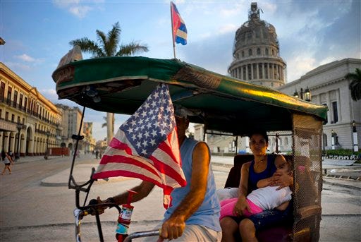 A taxi pedals his bicycle, decorated with Cuban and U.S. flags, as he transports a woman holding a sleeping girl, near the Capitolio in Havana, Cuba, Tuesday, March 15, 2016. President Barack Obama will travel to Cuba on March 20. (AP Photo/Ramon Espinosa)