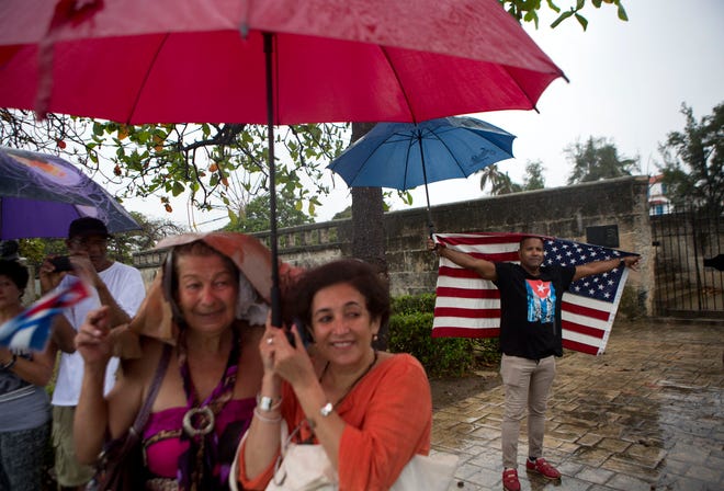 A handful of Cubans gather along the Malecon sea wall under a steady rain to wave to U.S. President Barack Obama's convoy before it arrives in Old Havana, Cuba, Sunday, March 20, 2016. Obama's trip is a crowning moment in his and Cuban President Raul Castro's ambitious effort to restore normal relations between their countries. (AP Photo/Rebecca Blackwell)