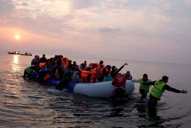 Volunteers help migrants and refugees on a dingy as they arrive at the shore of the northeastern Greek island of Lesbos, after crossing the Aegean sea from Turkey on Sunday. In another incident two Syrian refugees have been found dead on a boat on the first day of the implementation of an agreement between the EU and Turkey on handling the new arrivals. PETROS GIANNAKOURIS/THE ASSOCIATED PRESS