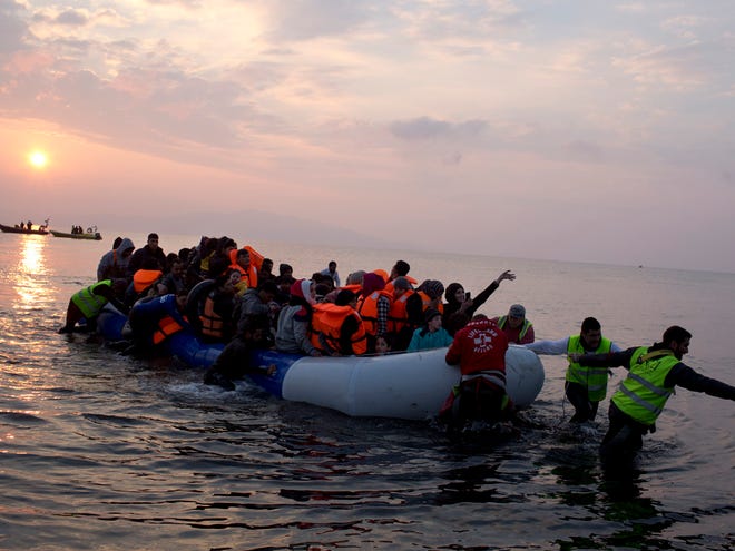 Volunteers help migrants and refugees on a dingy as they arrive at the shore of the northeastern Greek island of Lesbos, after crossing the Aegean sea from Turkey on Sunday, March 20, 2016. In another incident two Syrian refugees have been found dead on a boat on the first day of the implementation of an agreement between the EU and Turkey on handling the new arrivals.
