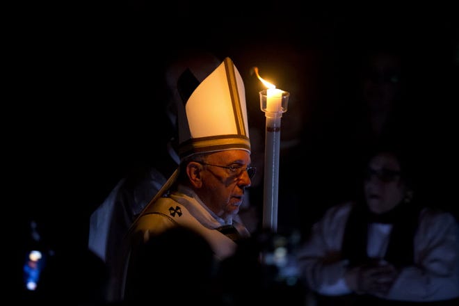 Pope Francis holds a lit white candle as he arrives for an Easter vigil service, in St. Peter's Basilica, at the Vatican, Saturday, April 4, 2015.
