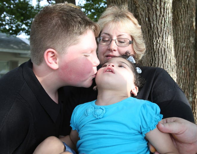 Natalya Potenza, 3, gets a kiss from her brother, Nathanial, 12, left, as she is held by her mother, Kelli Potenza, while they pose for photos at their home on Southeast 37th Terrace in Ocala, Fla. on Thursday, March 24, 2016. Christopher and Kelli Potenza have 5 adopted children who are all special needs children. This will be Natalya's first Easter with her adopted family. She was born to a drug addict mother and suffered an anoxic brain injury from being born a drug addict herself. She does not crawl or walk and is on a feeding tube. The family considers her their "Easter Blessing" this year.