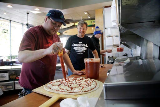 Chuck Hammers, owner of Pizza My Heart, center, watches as employee Tommy Selves, left, prepares a pizza Monday, March 28, 2016, in San Jose, Calif. A political deal to raise California's minimum wage to a nation-leading $15 an hour could help some workers cope with the state's crushing cost of living but also deprive other low-wage earners of jobs altogether, economists said Monday as Gov. Jerry Brown and other leaders touted what would be a landmark agreement. (AP Photo/Marcio Jose Sanchez)