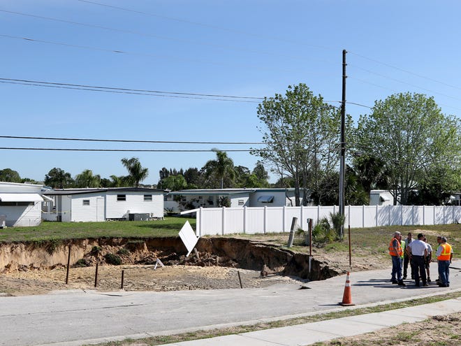 Emergency workers assess an area where a 60-foot-wide sinkhole opened on Wednesday in a Pinellas County utilities easement bordering the south side of the Tarpon Shores Mobile Home Park in Tarpon Springs.