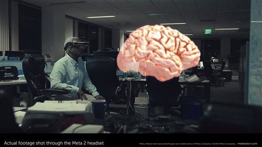 This February 2016 image provided by Meta shows actual footage of a model of a brain shot through the Meta 2 headset, while Meta employee Forest Rouse wears a Meta 2 headset, background left, in Redwood City, Calif. While startups like Meta, Magic Leap and Atheer have been making the most visible progress in augmented reality so far, technology heavyweights are also eyeing it. (Meta via AP) MANDATORY CREDIT