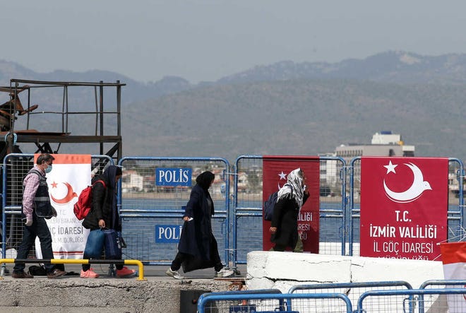 A Turkish police officer escorts migrants after a vessel transporting migrants from Greek island Chios docked in Dikili port, Turkey, Monday, April 4, 2016. A first group of migrants were ferried from the Greek islands to Turkey Monday as part of a controversial European Union plan to curb migration to Europe. Under heavy security, authorities on the Greek islands of Lesbos and Chios put 202 people on boats bound for Turkey - the first to be sent back as part of the plan, which has drawn strong criticism from human rights advocates. (AP Photo/Emre Tazegul)