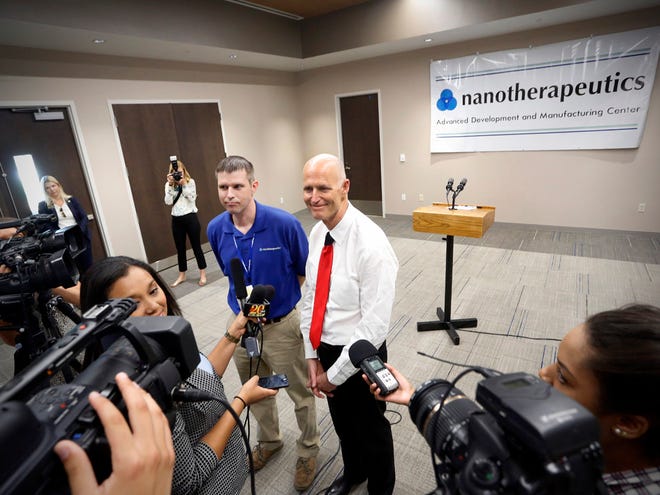 Florida Gov. Rick Scott, right, standing next to Jonah Goolsby, a controller at Nanotherapeutics Advanced Development and Manufacturing Center, holds a press conference discussing jobs made available at the facility in Alachua.