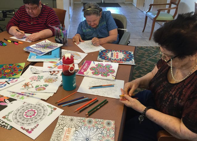 Heron East residents Ana Gonzales, left, Pat Anderson and Carol Weinberger get to work on pages from adult coloring books.