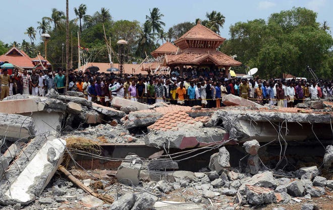 People gather near damaged buildings at the spot where a massive fire broke out during a fireworks display at the Puttingal temple complex in Paravoor village, Kollam district, southern Kerala state, India, Sunday, April 10, 2016. Dozens were killed and many more were injured when a spark from an unauthorized fireworks show ignited a separate batch of fireworks that were being stored at the temple complex, officials said.(AP Photo/ Jyothiraj. N.S)