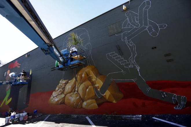 Artists paint murals on the side of Market Street Pub as part of the 352 Walls project.