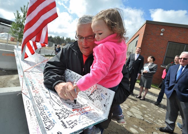 Paul Callinan of Holbrook is assisted by his granddaughter, Aria Callinan, 3, in signing the final beam for the new K-12 school during a topping of ceremony.
Wicked Local photo/Tom Gorman