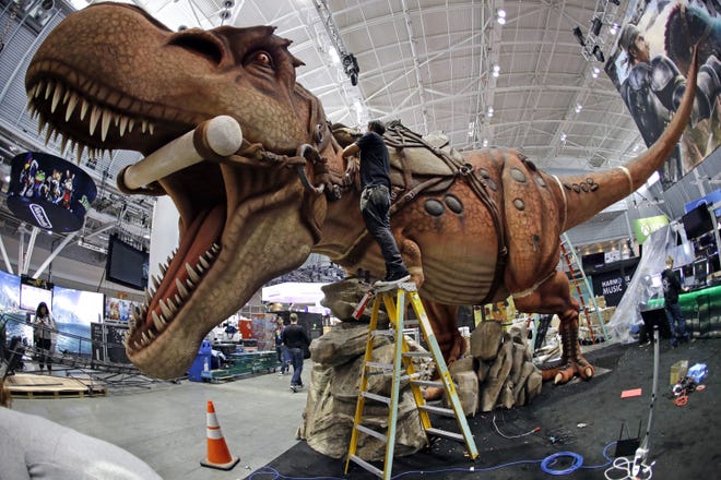 Joshua Patino stands on a ladder to put finishing touches on a giant dinosaur exhibit at PAX East in the Boston Convention and Expo Center Thursday. The annual celebration of gaming culture is expected to draw tens of thousands of visitors through Sunday. ELISE AMENDOLA/THE ASSOCIATED PRESS